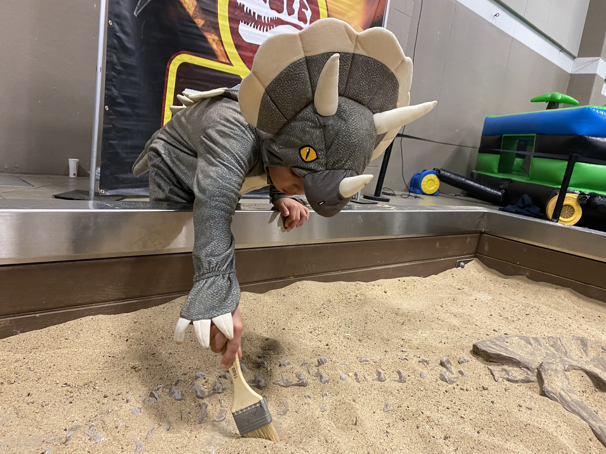 child with dinosaur headdress digging in sandbox