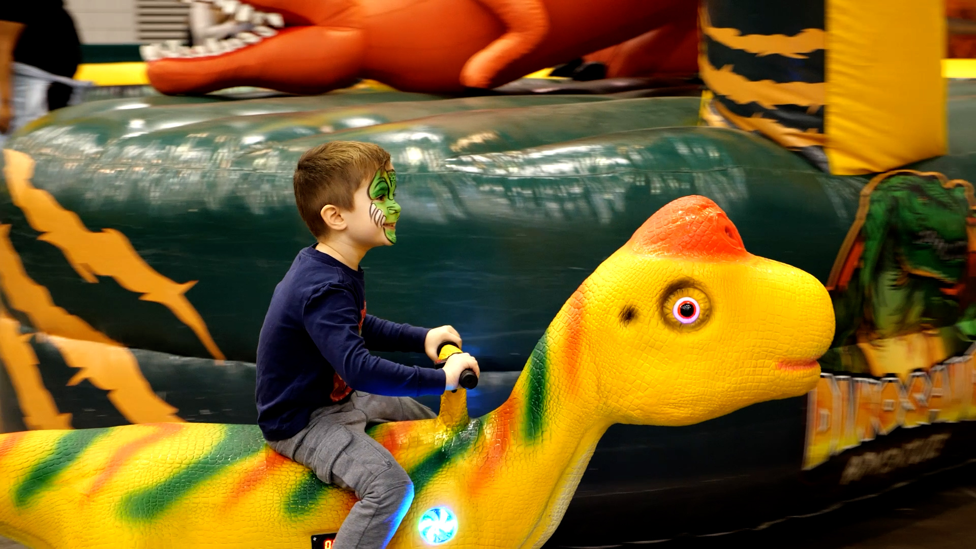 child with dinosaur painted face on dinosaur ride